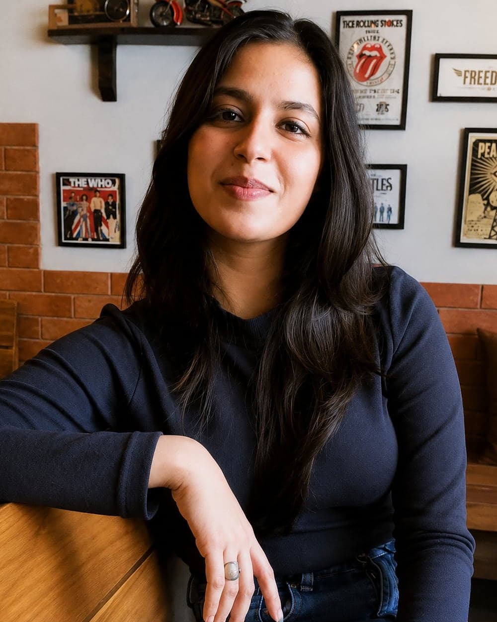 Akanksha Verma, Manager of Human Resources at Pelocal, leaning on a bench in front of a wall of framed posters.